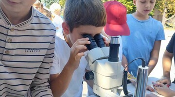 Dzieci odwiedzające stoisko, chłopiec patrzy przez mikroskop