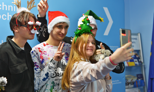 Grupa studentów zagranicznych w przebraniach świątecznych przy choince robiąca zdjęcie